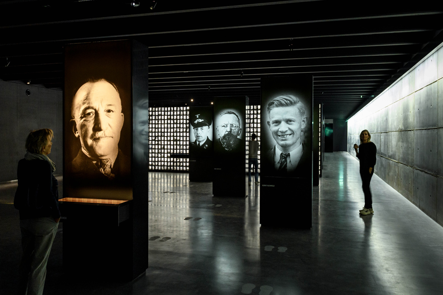 Ondergrondse permanente tentoonstellingsruimte met herinneringszuilen en de portrettenwand op de achtergrond